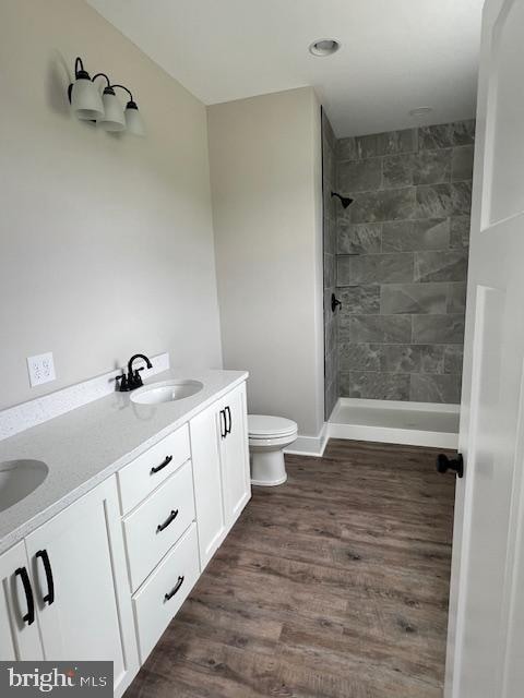 bathroom with vanity, toilet, hardwood / wood-style flooring, and a tile shower