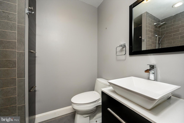 full bathroom featuring a tile shower, toilet, vanity, and baseboards