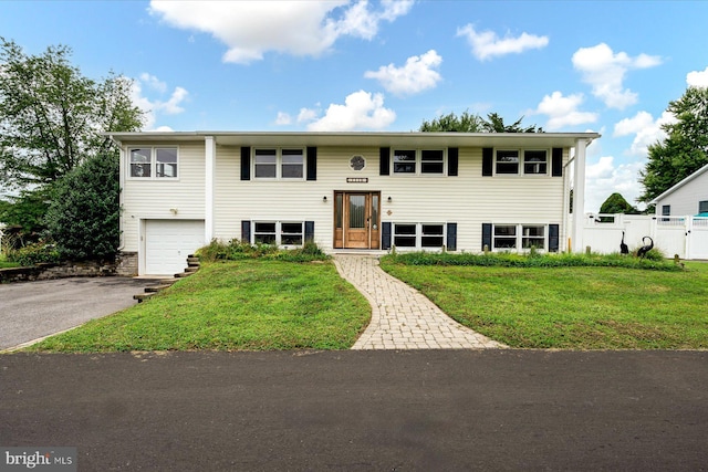 split foyer home featuring an attached garage, a front yard, aphalt driveway, and fence