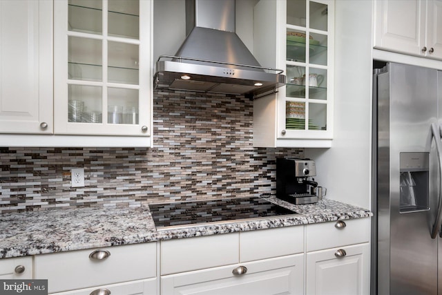 kitchen featuring wall chimney exhaust hood, stainless steel refrigerator with ice dispenser, white cabinets, and black stovetop