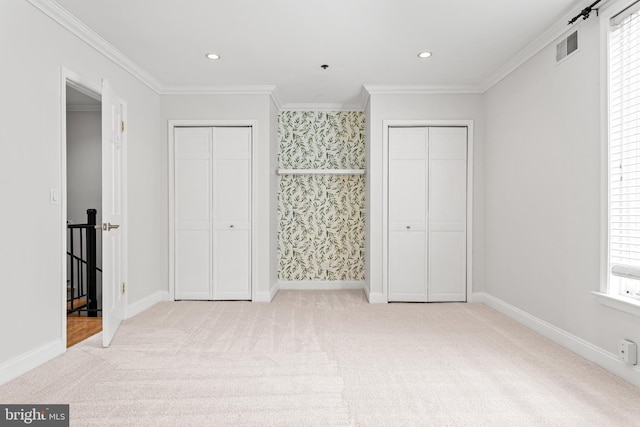 unfurnished bedroom with crown molding, two closets, and light carpet