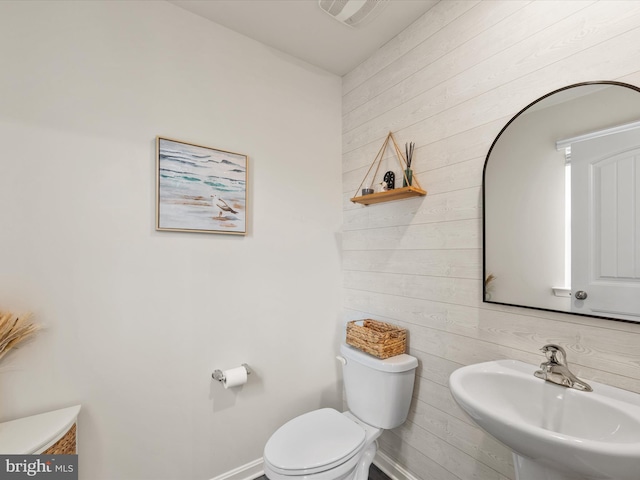 bathroom featuring wood walls, toilet, and sink