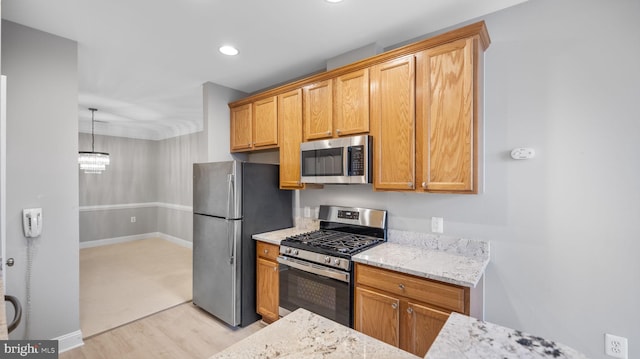 kitchen with light stone countertops, stainless steel appliances, decorative light fixtures, and light hardwood / wood-style floors