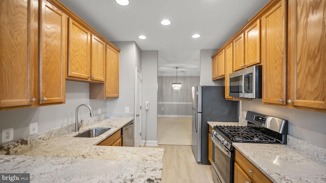 kitchen with light stone countertops, sink, light hardwood / wood-style floors, decorative light fixtures, and appliances with stainless steel finishes