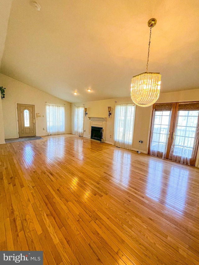 unfurnished living room with vaulted ceiling, light hardwood / wood-style flooring, and a chandelier