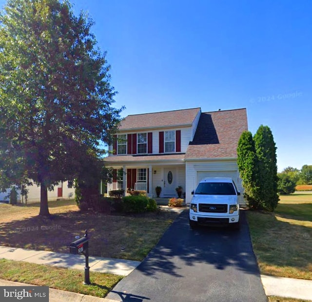 colonial inspired home featuring a garage, covered porch, and a front yard