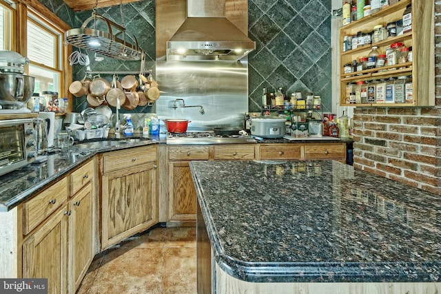 kitchen with dark stone counters, stainless steel gas cooktop, and wall chimney range hood