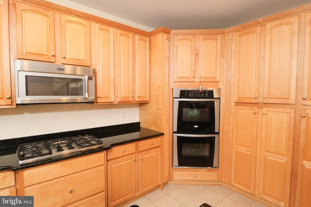 kitchen with dark stone counters, light brown cabinets, appliances with stainless steel finishes, and light tile patterned floors