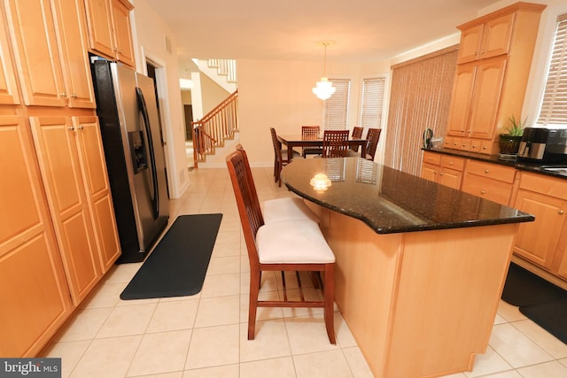 kitchen featuring dark stone counters, stainless steel fridge with ice dispenser, a kitchen island, decorative light fixtures, and light tile patterned floors