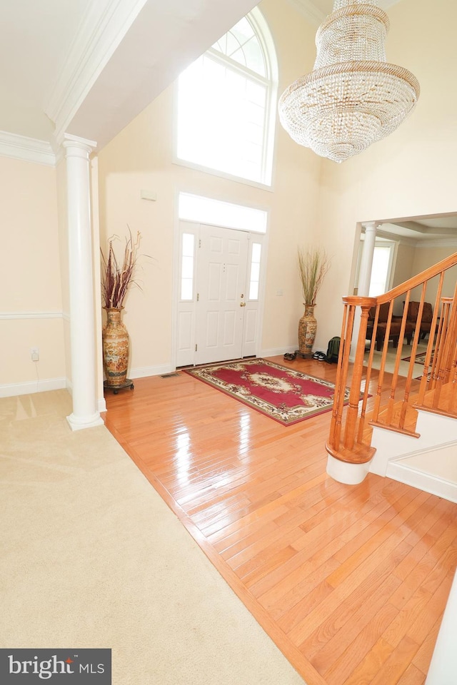 foyer entrance featuring wood-type flooring, a high ceiling, crown molding, an inviting chandelier, and decorative columns