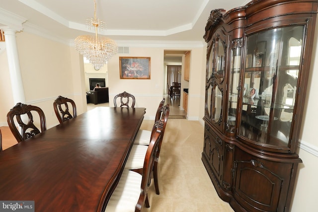 carpeted dining area featuring a notable chandelier, a tray ceiling, decorative columns, and crown molding