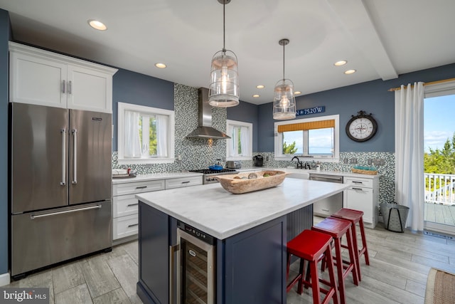 kitchen featuring a healthy amount of sunlight, beverage cooler, appliances with stainless steel finishes, and wall chimney range hood