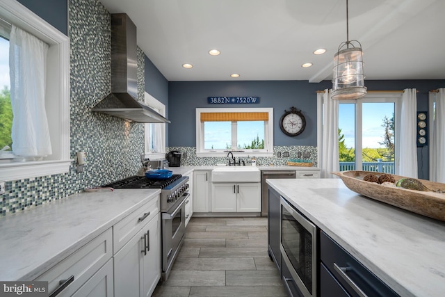 kitchen featuring sink, white cabinetry, wall chimney exhaust hood, stainless steel appliances, and decorative light fixtures