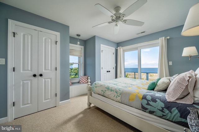 carpeted bedroom with ceiling fan, multiple closets, and a water view