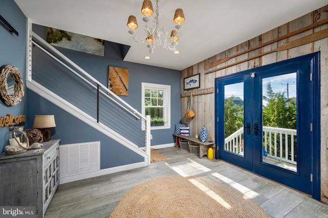 entryway with wood-type flooring, wood walls, a chandelier, and french doors