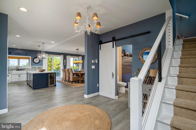 interior space featuring wine cooler, light hardwood / wood-style floors, sink, a barn door, and an inviting chandelier