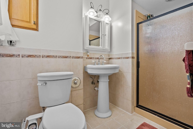 bathroom with toilet, a shower with shower door, tile walls, and tile patterned flooring