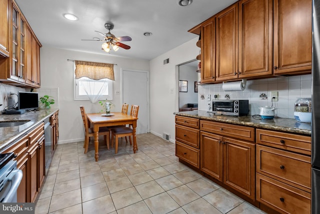 kitchen featuring stainless steel appliances, dark stone counters, light tile patterned flooring, tasteful backsplash, and ceiling fan