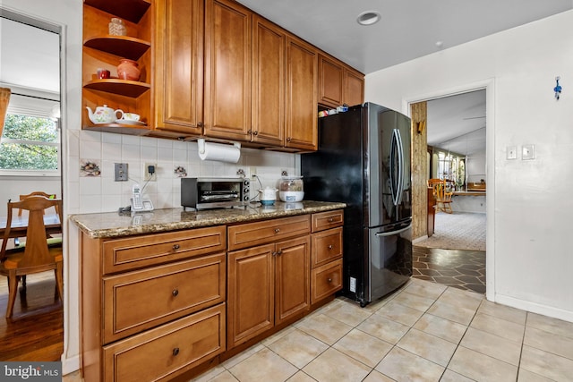 kitchen featuring stone countertops, decorative backsplash, light tile patterned floors, and black refrigerator