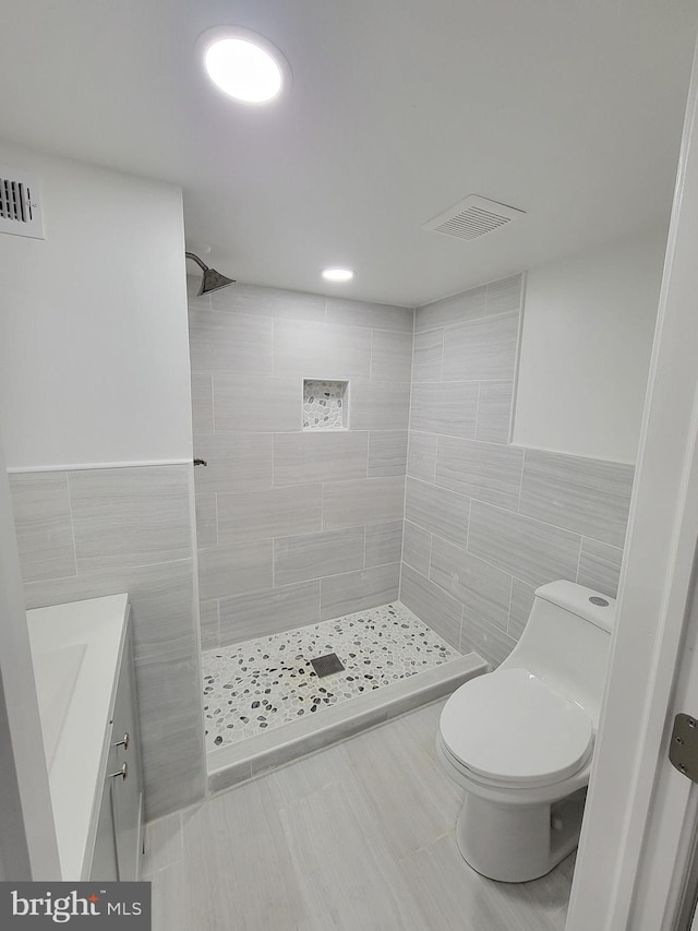 bathroom featuring tile walls, tiled shower, vanity, and toilet