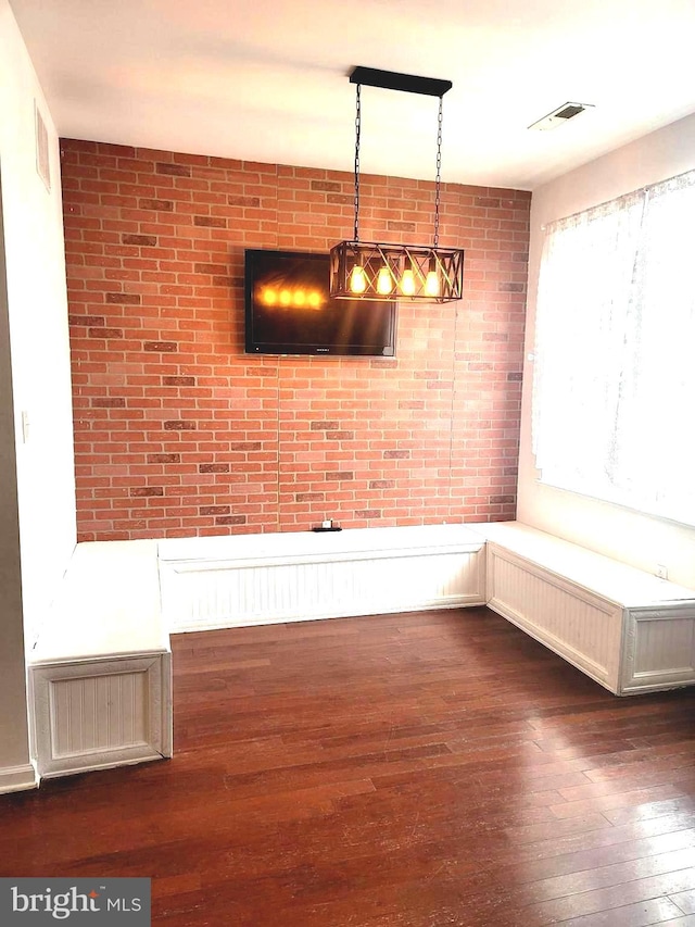 unfurnished dining area featuring brick wall and dark hardwood / wood-style flooring