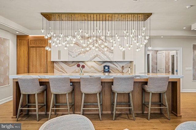 bar with decorative light fixtures, backsplash, and light hardwood / wood-style floors