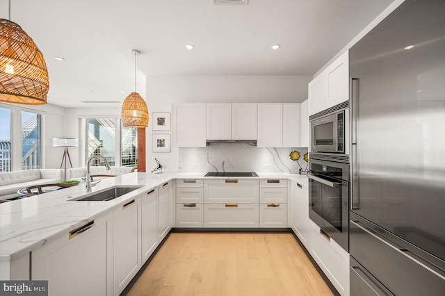 kitchen featuring appliances with stainless steel finishes, white cabinetry, pendant lighting, light wood-type flooring, and sink