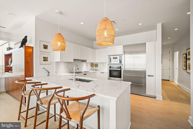 kitchen with hanging light fixtures, light hardwood / wood-style floors, kitchen peninsula, built in appliances, and a kitchen bar