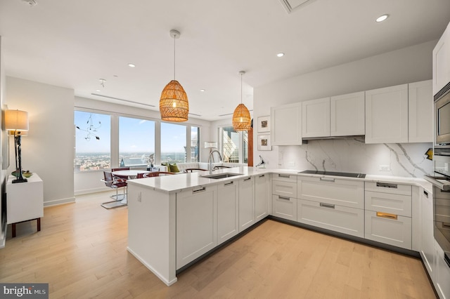 kitchen with hanging light fixtures, light hardwood / wood-style floors, white cabinetry, kitchen peninsula, and sink