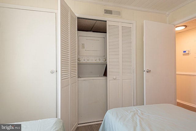 bedroom featuring stacked washing maching and dryer, hardwood / wood-style floors, and crown molding