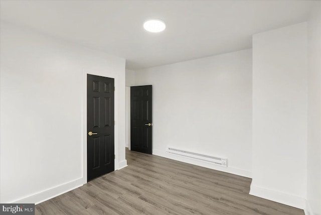 spare room featuring a baseboard heating unit and hardwood / wood-style flooring