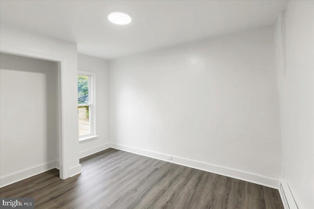 unfurnished room with dark wood-type flooring and a baseboard heating unit