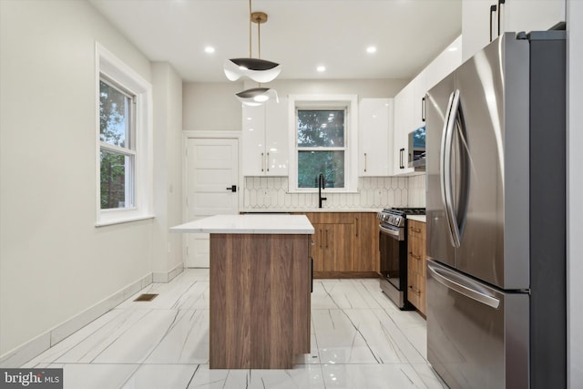 kitchen featuring white cabinets, a kitchen island, decorative light fixtures, appliances with stainless steel finishes, and decorative backsplash