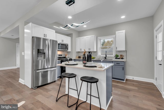 kitchen with appliances with stainless steel finishes, white cabinetry, light wood-type flooring, a center island, and sink