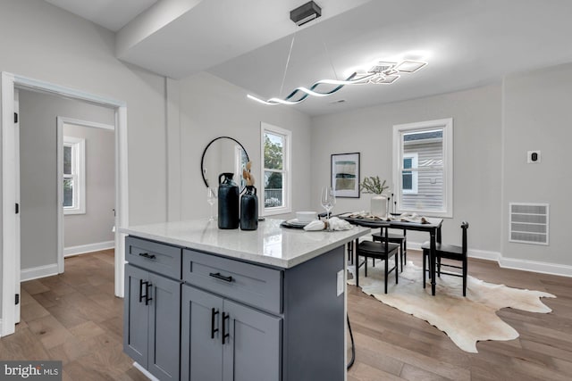 kitchen featuring light stone countertops, gray cabinetry, a kitchen island, and hardwood / wood-style floors