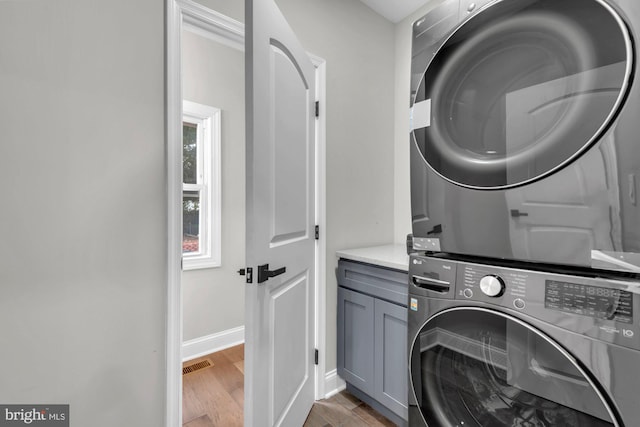 laundry room featuring cabinets, dark hardwood / wood-style floors, and stacked washer and clothes dryer