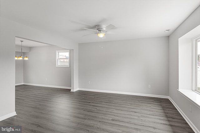 empty room featuring ceiling fan with notable chandelier and dark wood-type flooring