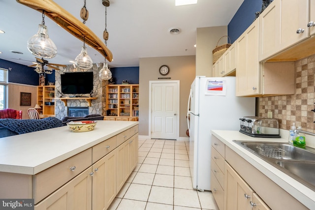 kitchen featuring white refrigerator, light tile patterned floors, tasteful backsplash, a stone fireplace, and decorative light fixtures