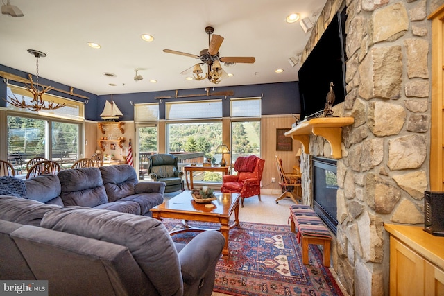 living room featuring a stone fireplace, carpet flooring, and ceiling fan