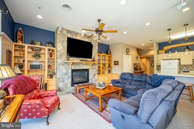 carpeted living room with ceiling fan and a stone fireplace