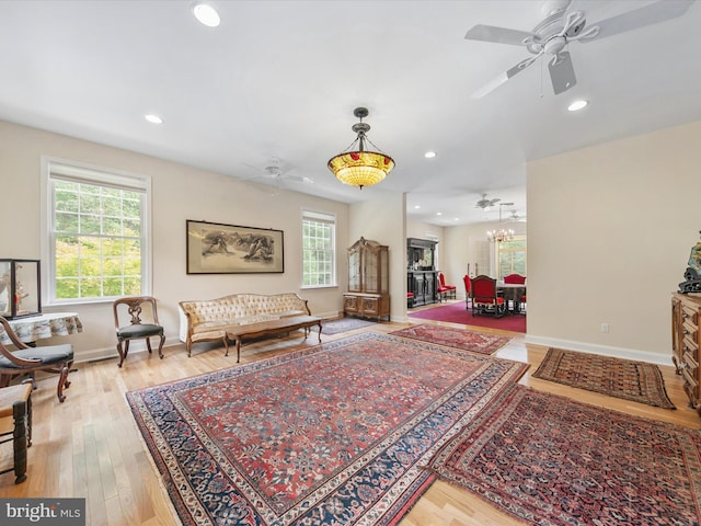 sitting room with ceiling fan with notable chandelier, light wood-type flooring, and a wealth of natural light