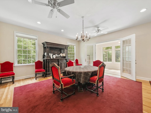 dining space with hardwood / wood-style flooring, ceiling fan with notable chandelier, a wealth of natural light, and french doors