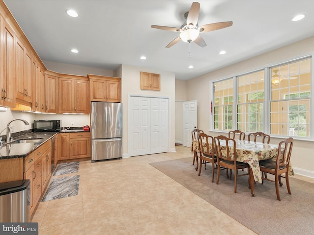 kitchen featuring stainless steel refrigerator, ceiling fan, sink, dishwasher, and dark stone counters