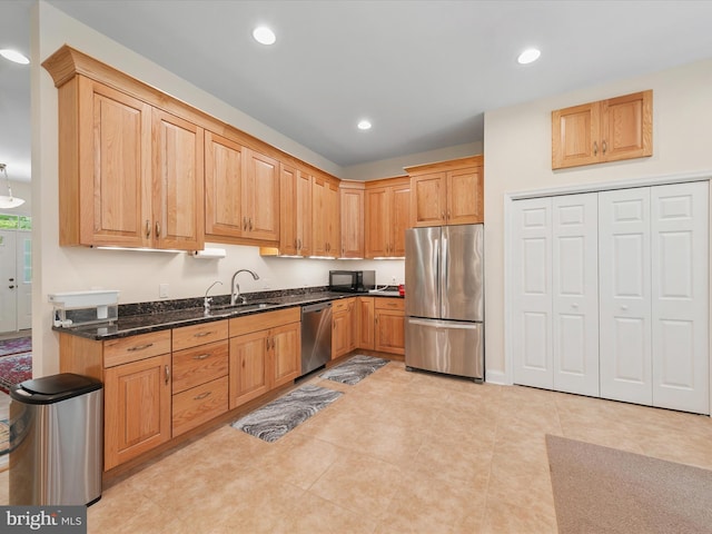 kitchen featuring light tile patterned floors, stainless steel appliances, dark stone countertops, and sink