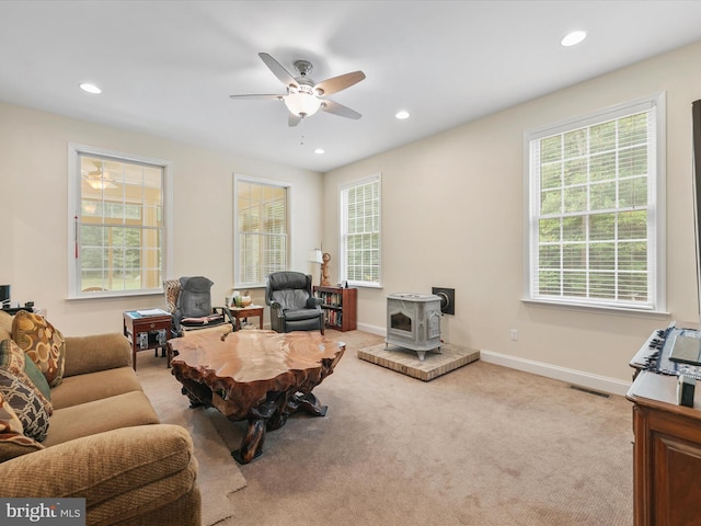 carpeted living room with a wood stove, a wealth of natural light, and ceiling fan