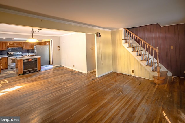 unfurnished living room with wooden walls, dark hardwood / wood-style floors, sink, and crown molding