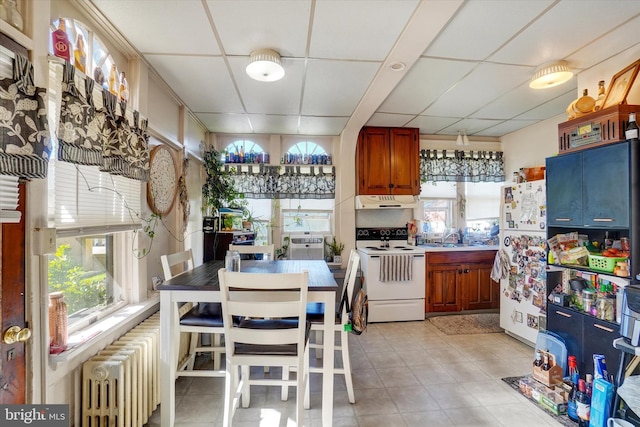 kitchen featuring radiator heating unit, white appliances, light tile patterned floors, and a paneled ceiling