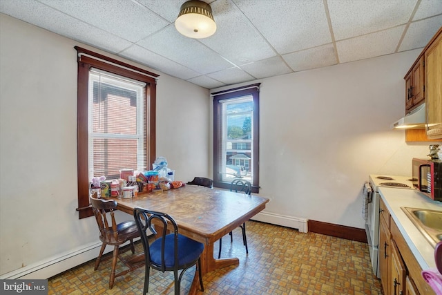 dining space with a baseboard heating unit, a drop ceiling, and a healthy amount of sunlight