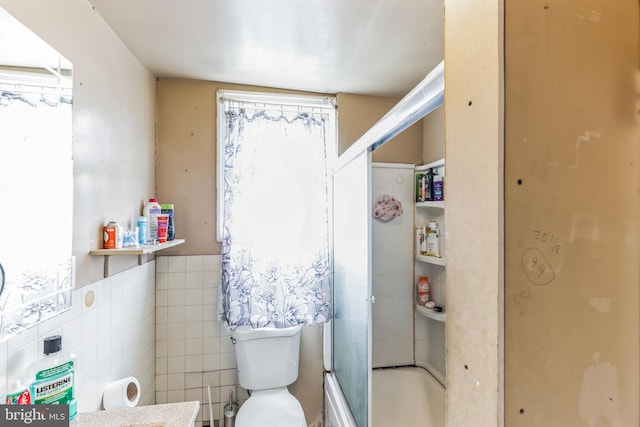 bathroom featuring tile walls, bath / shower combo with glass door, and toilet