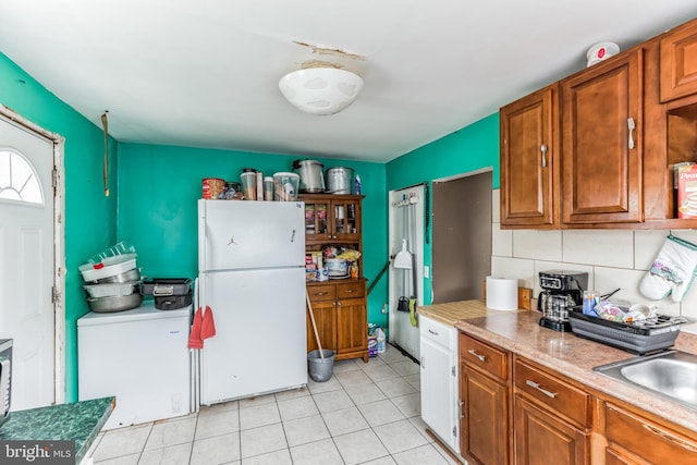 kitchen with white refrigerator, backsplash, light tile patterned floors, fridge, and sink